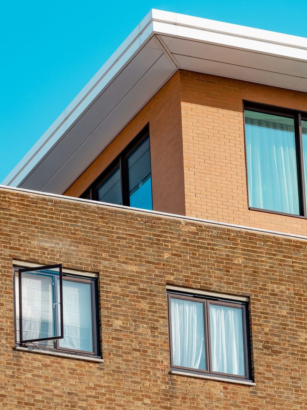 Modern brick building with large windows and an open window against a clear blue sky.